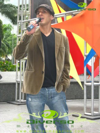 Roman EL RO singing into a microphone at an outdoor benefit event.